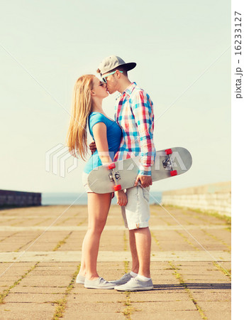 smiling couple with skateboard kissing outdoors 16233127