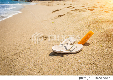 slippers and sunblock lotion lying on seashore 16287887