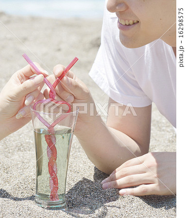 ビーチで寄り添いハート型のストローでドリンクを飲む男性の写真素材