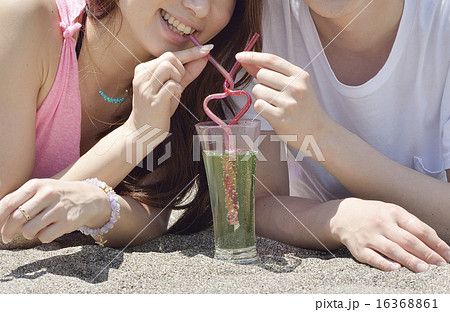 ビーチで寄り添いハート型のストローでドリンクを飲むカップルの写真素材