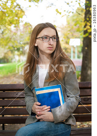Thoughtful student with glasses sitting on bench 16380963