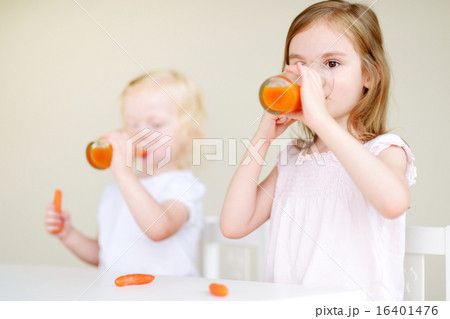 Two cute little sisters drinking carrot juice 16401476