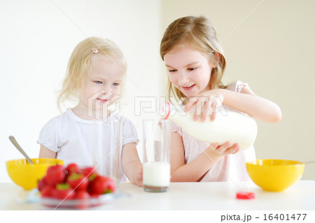 Two cute little sisters eating cereal in a kitchen 16401477