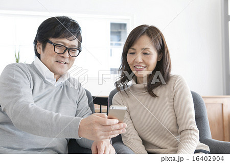 自宅でスマホをみるシニア世代の夫婦 16402904