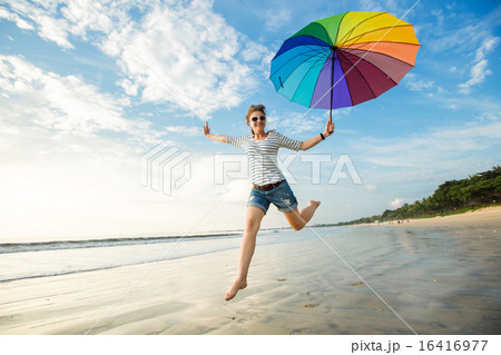 Cheerful young girl with rainbow umbrella having fun on the beach before sunset. Travel, holidays Cheerful young girl with rainbow umbrella having fun on the beach before sunset. Travel, holidays 16416977