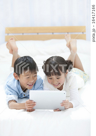 ベッドに寝転んでタブレットPCを見る子供たち 16417166