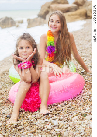 Two cute smiling girls are sitting on the beach 16585366