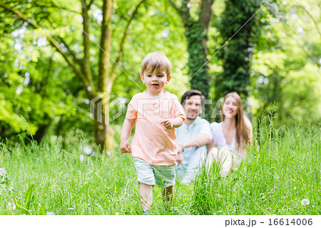 Little boy running over meadow with family in back 16614006