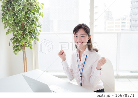 オフィス窓際でパソコンの前でガッツポーズをして喜ぶ若い女性 Olの写真素材