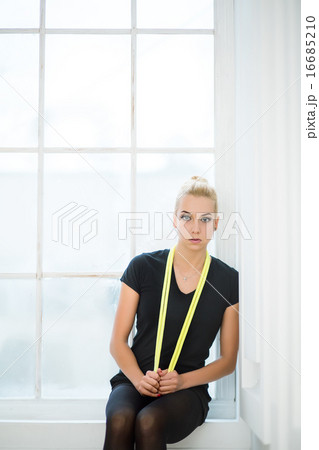 Rhythmic gymnast sitting with yellow rope slung over the neck 16685210
