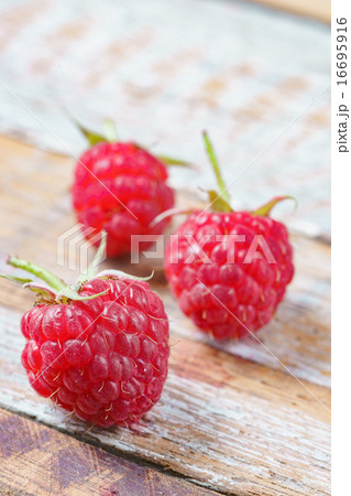Three red raspberry on old vintage wooden table. 16695916