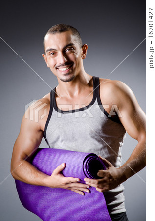 Muscular man with mat in studio 16701427