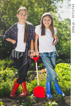 girls in rubber boots posing at garden with shovel 16722582