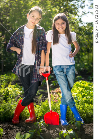 Two girls in gumboots posing with shovel on garden 16722583