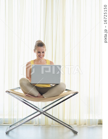 Happy young woman sitting on modern chair with laptop Happy young woman sitting on modern chair with laptop 16725150
