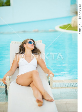 Young woman laying on chaise-longue at poolside 16725548