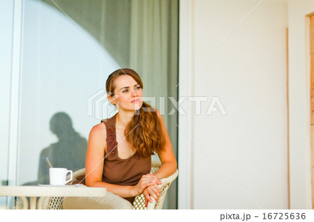 Thoughtful young female sitting on terrace with cup of tea and 16725636