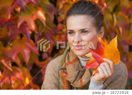 Portrait of thoughtful young woman with autumn leafs in front of 16725916