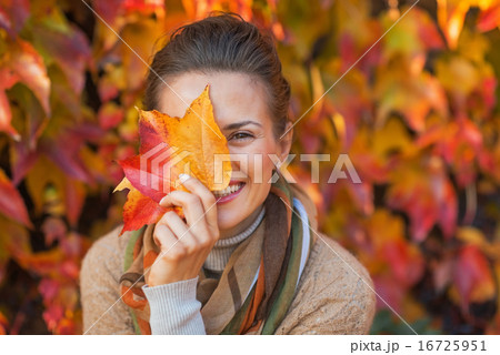 Portrait of happy young woman hiding behind autumn leafs in fron 16725951