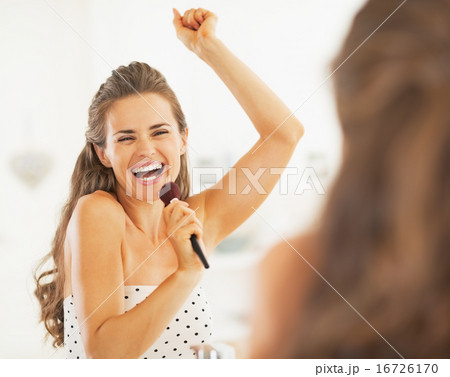 Happy young woman singing in makeup brush in bathroom Happy young woman singing in makeup brush in bathroom 16726170