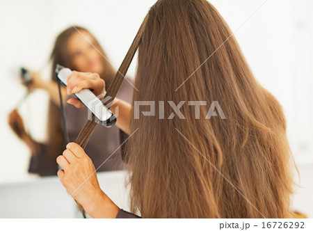 Woman straightening hair with straightener . rear view 16726292