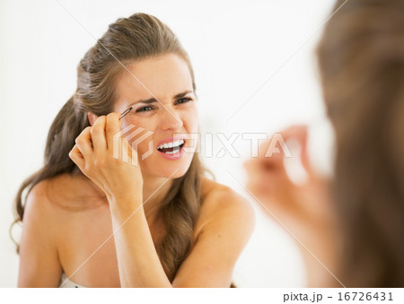 Displeased young woman tweezing eyebrows 16726431
