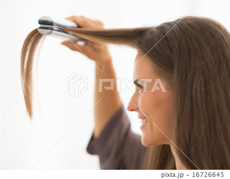 Young woman straightening hair in bathroom 16726645
