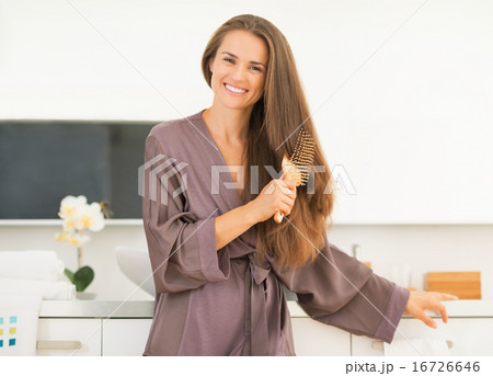 Happy young woman combing hair in bathroom 16726646