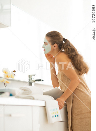 Young woman wearing facial cosmetic mask in bathroom looking in Young woman wearing facial cosmetic mask in bathroom looking in 16726698