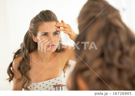 Portrait of young woman checking facial skin condition 16726905