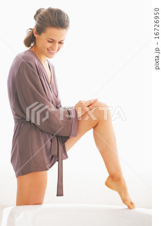 Young woman applying cream on leg in bathroom Young woman applying cream on leg in bathroom 16726950