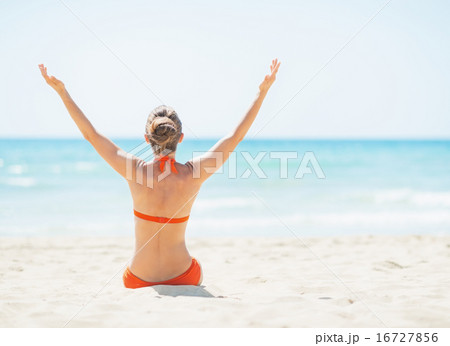 Young woman sitting on beach and rejoicing. rear view 16727856