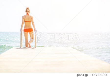 Young woman going down into sea from bridge. rear view Young woman going down into sea from bridge. rear view 16728083