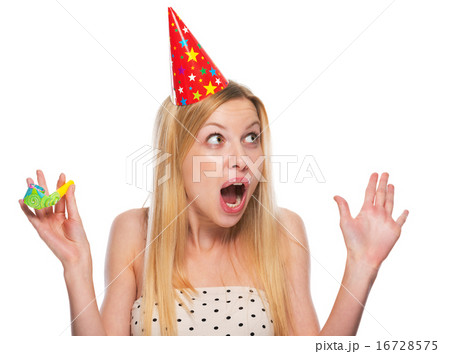 Portrait of surprised teenage girl in cap with party horn blower 16728575