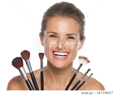 Smiling young woman holding makeup brushes 16728857