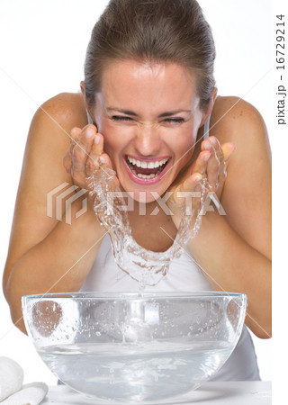 Happy young woman washing face in glass bowl with water 16729214