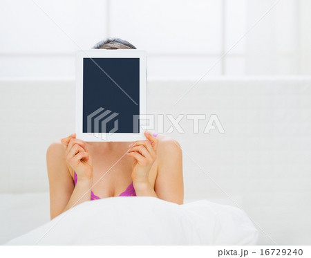 Woman sitting in bed and hiding tablet PC in front of face Woman sitting in bed and hiding tablet PC in front of face 16729240