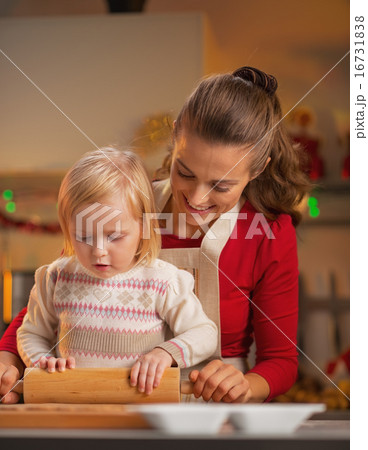 Mother and baby rolling pin dough in christmas decorated kitchen 16731838