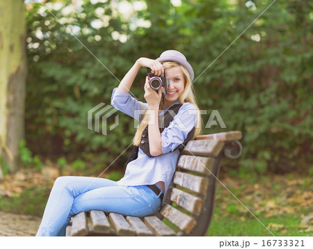 Young hipster taking photo with retro photo camera sitting on be 16733321