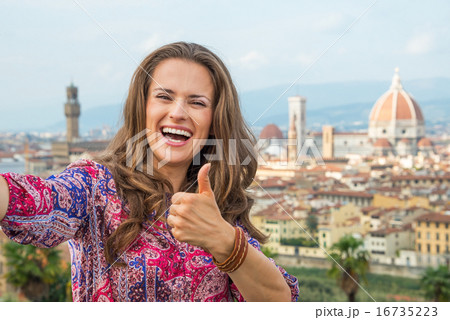 Happy young woman making selfie and showing thumbs up against pa Happy young woman making selfie and showing thumbs up against pa 16735223