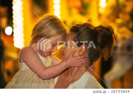 Portrait of mother and baby girl hugging in front of carousel Portrait of mother and baby girl hugging in front of carousel 16735644