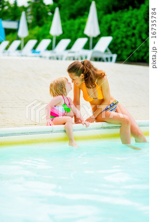 Happy mother and baby girl sitting at poolside 16735784
