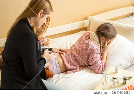 Mother making injection in sick girl's bottom on b 16746686