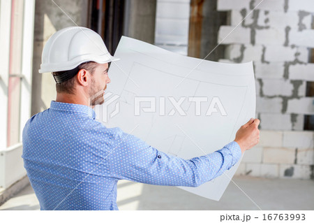 Cheerful young builder is studying the layout of new project Cheerful young builder is studying the layout of new project 16763993