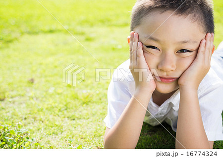 芝生で頬杖をつきおどける子ども の写真素材
