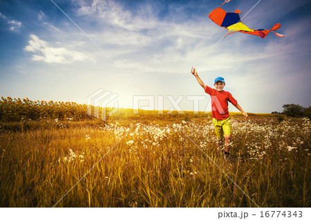 Boy running across the field with kite flying over his head Boy running across the field with kite flying over his head 16774343