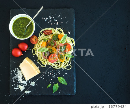 Spaghetti with pesto sauce, roasted cherry-tomatoes, fresh basil and parmesan cheese on black stone 16779424