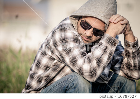 Portrait of a sad man in sunglasses sitting near the house 16787527