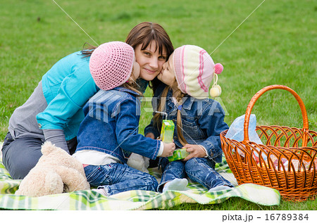 Two daughters kissing mother while on a picnic Two daughters kissing mother while on a picnic 16789384