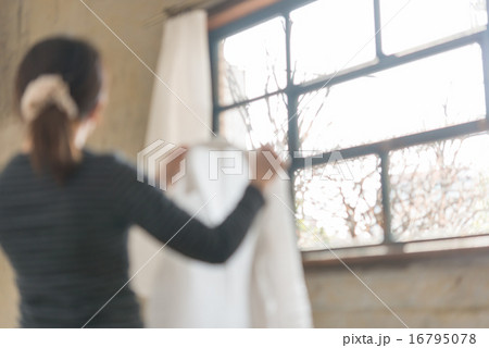 窓辺でカーテンを開ける女性、光が差し込む室内 16795078